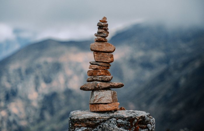 Balanced stones forming a cairn against a tranquil mountain backdrop under a cloudy sky.