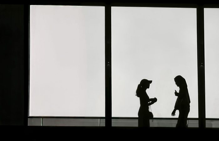 Silhouetted view of two individuals interacting indoors against a bright window.