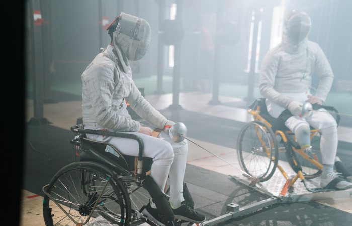Two male wheelchair fencers practicing in a gym, focusing on training and skill development.