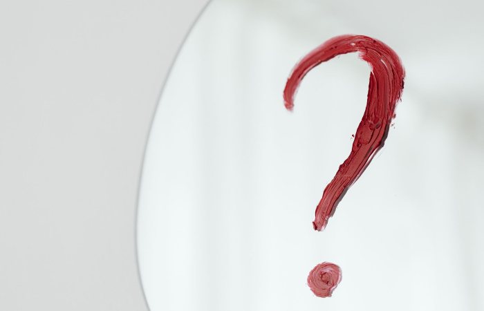 Close-up of a red question mark painted on a mirror with a white background.