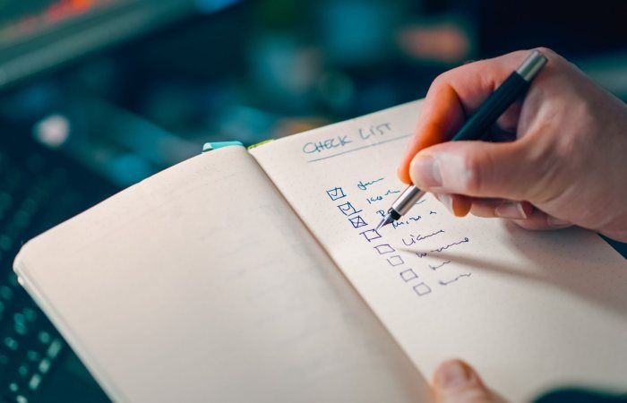 Close-up of a hand writing in a notebook with a checklist for effective task management.