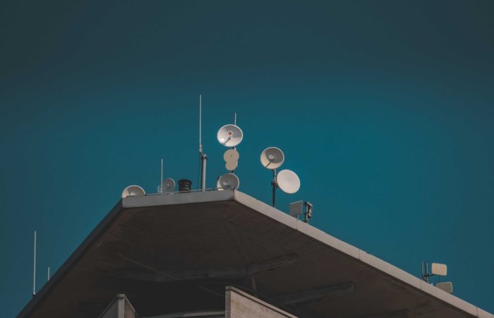 A low-angle view of communication dishes and antennas on a building against a clear blue sky.